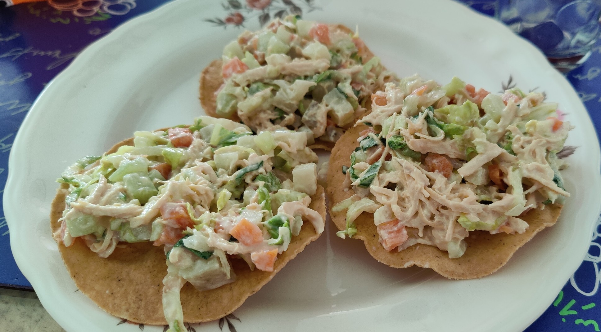 3 salad’s tostadas on top of a white dish. The salad has a mixed texture and colorful white-ish aspect due to the chopped vegetables and the creme.
